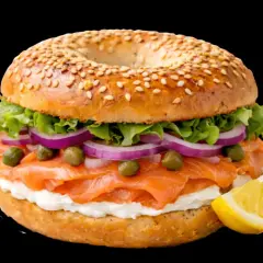 Un délicieux bagel saumon garni de fromage frais, oignons rouges, câpres et laitue, avec un quartier de citron à côté.