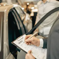 Mężczyzna w garniturze podpisuje dokument "CAR RENTAL" przy luksusowym samochodzie.