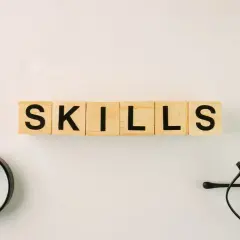 Wooden blocks spell "SKILLS." A magnifying glass and glasses suggest an organization leader carefully assessing talents.