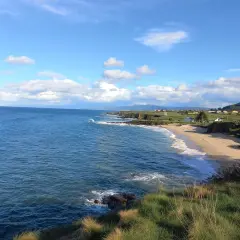Mar azul y cielo nublado sobre la playa de Xuncos, con casas dispersas en la costa verde.