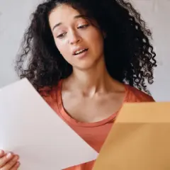 Jeune femme perplexe devant sa lettre de motivation Parcoursup. Elle tient un document blanc et une enveloppe marron.