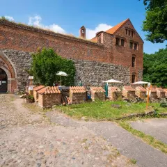 Kamienne mury i ceglane budynki zamku bierzgłowskiego, z bramą i zielenią.