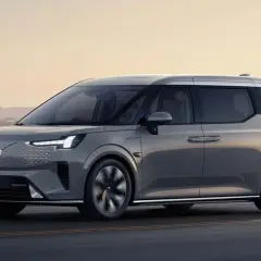 Szary Volvo EM90 jedzie wzdłuż wybrzeża o zachodzie słońca.