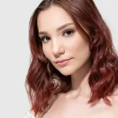 Portret młodej kobiety z falowanymi, mahoniowo-brązowymi włosami.