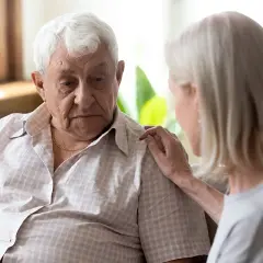 Starszy mężczyzna zmartwiony, kobieta kładzie mu dłoń na ramieniu, wspierając go w walce z objawami psychozy.