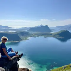 Kvinna sitter på klippavsats med fantastisk utsikt över fjordlandskap på Lofoten.
