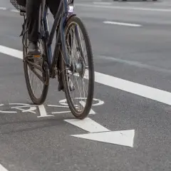 Rowerzysta na ścieżce rowerowej z białymi oznaczeniami kierunku jazdy.