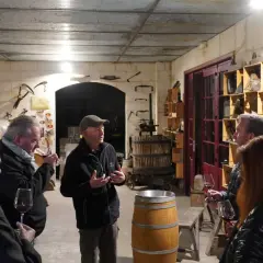Visite d'une cave à vin du Médoc. Un guide explique la fabrication du vin à des visiteurs, entourés de fûts et d'outils anciens.