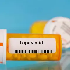 Orange pill bottle with "Loperamid" label and yellow pills inside. Another blurred bottle in the background.