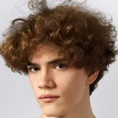 Joven con pelo castaño rizado y voluminoso, un estilo moderno que realza sus rasgos. Cortes pelo rizado hombre.
