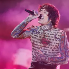Oli Sykes z Bring Me The Horizon Polska śpiewa na koncercie, ubrany w koszulkę z tatuażami i francuskim tekstem.