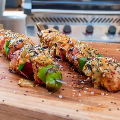 Fertige Schaschlik-Spieße mit Sauce und Sesam auf einem Holzbrett, bereit für den Schaschlik Grill.