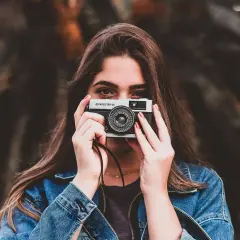 Młoda kobieta z aparatem Olympus Trip 35, gotowa do zrobienia zdjęcia. Wzór umowy z fotografem czeka na podpis.