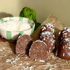 Hemmagjorda delicatobollar, täckta med choklad och kokosflingor, redo att avnjutas. En skål med kokosflingor står bredvid.