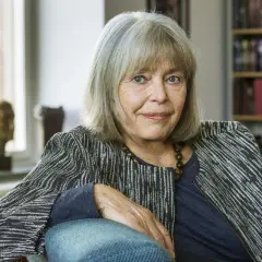 Agneta Pleijel, författare, sitter i en fåtölj med en bokhylla i bakgrunden.