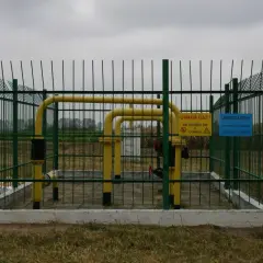 Ogrodzony obiekt gazowy z żółtymi rurami. Tablice ostrzegawcze informują o zagrożeniu i numerach alarmowych. Widać, że odległość budynku od gazociągu średniego ciśnienia jest bezpieczna.
