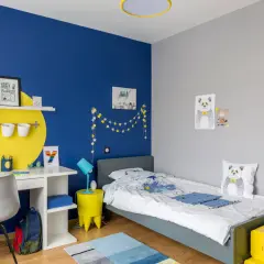 Cameretta con parete blu vivace e decorazioni a stelle. Scrivania bianca, letto grigio, cuscino panda. Ottime idee pittura cameretta per un ambiente allegro.
