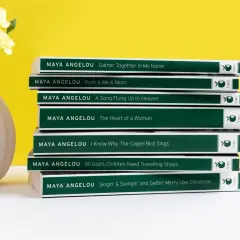 Stos **książek** **Maya Angelou** obok wazonu z żółtymi kwiatami.