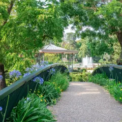Un pont fleuri mène à un kiosque et une fontaine au jardin des plantes de Toulouse.