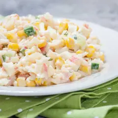 Deliciosa ensalada de arroz con mayonesa, maíz, pepino y surimi, servida en un plato blanco sobre una servilleta verde.