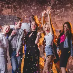 Grupa młodych ludzi świętuje, sypią się konfetti. Inspiracja, jak się ubrać do klubu: sukienki, jeansy, marynarki.