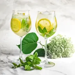 Orzeźwiający drink z prosecco i sokiem z bzu, ozdobiony plasterkami cytryny i listkami mięty, z lodem.
