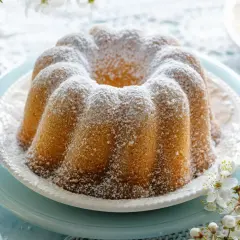 Puszysta babka cytrynowa oprószona cukrem pudrem, ozdobiona gałązką kwitnącej wiśni. Idealna na wiosenne popołudnie.