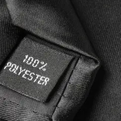 Czarna metka z napisem "100% POLYESTER" na tle eleganckiej tkaniny. Czy poliester się rozciąga? Ten materiał wygląda na wytrzymały.