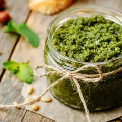 Słoik domowego pesto, ozdobiony sznurkiem, z orzeszkami pinii i listkami bazylii. Idealny przepis, jak zrobić pesto.