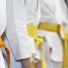 Zbliżenie na białe kimona z pomarańczowym i żółtym pasem, symbolizujące sztuki walki.