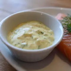 En skål med krämig gravlaxsås enkel, med dill och senapsfrön, bredvid en bit lax.
