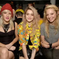 Tres jóvenes con un estilo que evoca el "heroin chic" posan juntas. Una lleva un gorro rojo, otra una chaqueta colorida y la tercera una camiseta gris.