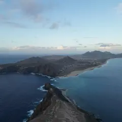 Dramatic coastline of Porto Santo island, with rugged cliffs meeting turquoise waters and a long sandy beach stretching towards distant mountains under a cloudy sky.