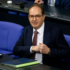 Ein Mann mit Brille und Krawatte sitzt im Bundestag. Er wirkt nachdenklich, während er seine Hände faltet. Viele Bundestagsabgeordnete sind Beamte.