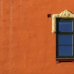 Ett fönster med en utsmyckad, gul ram på en orange, målad putsad fasad.
