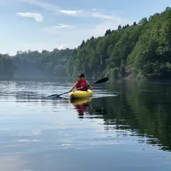 Person in gelbem Kajak genießt eine friedliche Kanu fahrt auf einem ruhigen See, umgeben von üppigen grünen Wäldern.