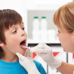 Lekarz od uszu bada gardło chłopca.