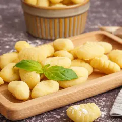 Pyszne, domowe gnocchi na drewnianej desce, gotowe na pyszny sos. Obok czosnek i świeża bazylia. Idealny przepis na gnocchi z sosem.