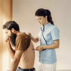 Médica examina a un hombre con barba que tose, sintiendo su espalda. Podría tener dolor de espalda al toser.