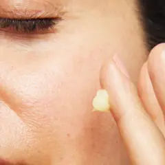 Närbild på en persons ansikte med slutna ögon. Ett finger med en klick kräm, kanske för att visa retinol resultat.