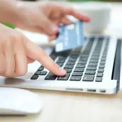 Dłoń z kartą zbliża się do klawiatury laptopa, gotowa do płatności. To jak szybkie przelewy przez Skrill, wygodne i bezpieczne.