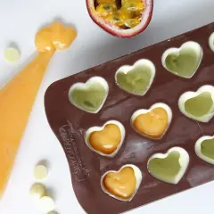 Gör egna enkla chokladpraliner recept med passionsfrukt och vit choklad i hjärtformad form. En påse med orange fyllning ligger bredvid.