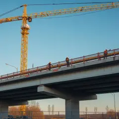 Pracownicy na budowie mostu, pod wielkim żółtym dźwigiem. Ich stawka godzinowa na budowie zależy od wielu czynników.