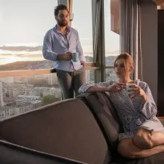 Para młoda pije kawę, podziwiając widok z okna. Penthouses co to? Luksusowe mieszkania na najwyższych piętrach.