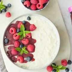 Cremiger Milchreis ohne Zucker, garniert mit frischen Himbeeren, Blaubeeren und Minze. Dazu eine Flasche zuckerarmer Himbeer-Fruchttoppping.