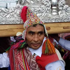 Kolorowy strój i tradycyjna czapka zdobią jednego z mężczyzn niosących ozdobną ramę. To **Indianie z Cuzco** podczas uroczystości.