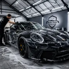 Mężczyzna myje czarne izera auto w garażu. Piana pokrywa lśniący lakier, zapowiadając perfekcyjne wykończenie.