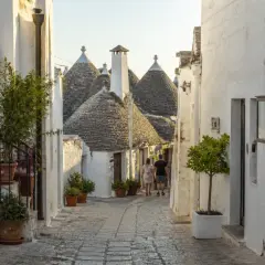 Ruelle pavée bordée de maisons blanches aux toits coniques typiques des Pouilles à éviter, avec un couple se promenant.