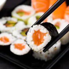 Chopsticks podnoszą kawałek sushi z łososiem. Czy sushi jest zdrowe? Tak, jeśli jest przygotowane z ryżu, ryb i warzyw.