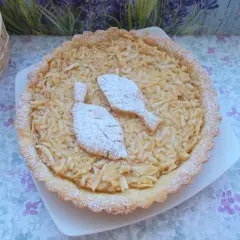 Pyszna tarta z jabłkami, posypana cukrem pudrem, z dwoma listkami z ciasta na wierzchu. Idealna na deser.